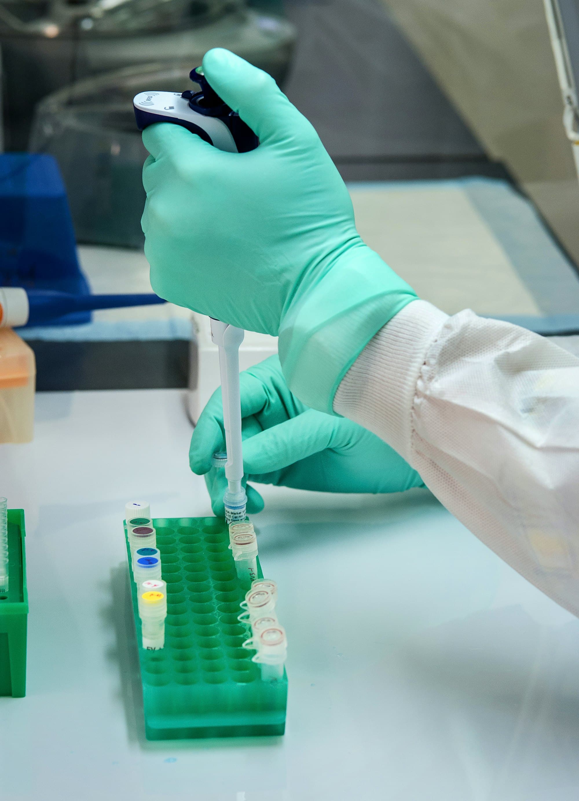Gloved hand pipetting liquid into small vials in a lab
