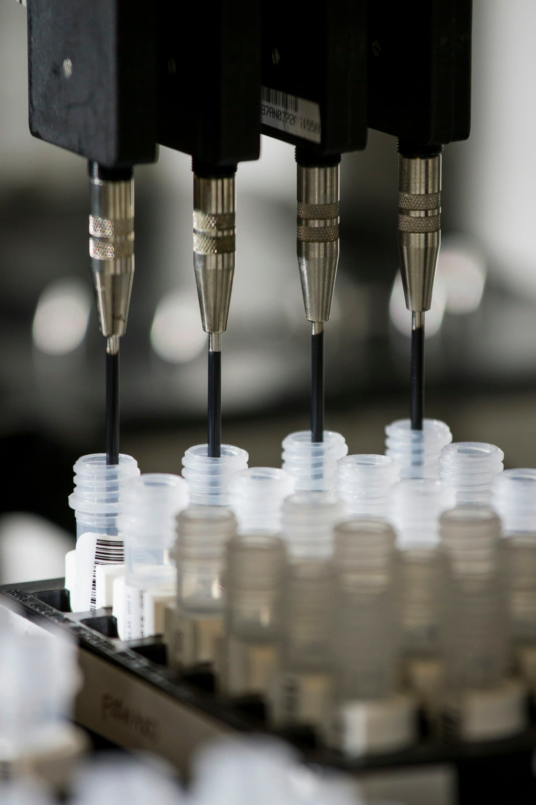 Needles dispensing liquid into rows of small vials